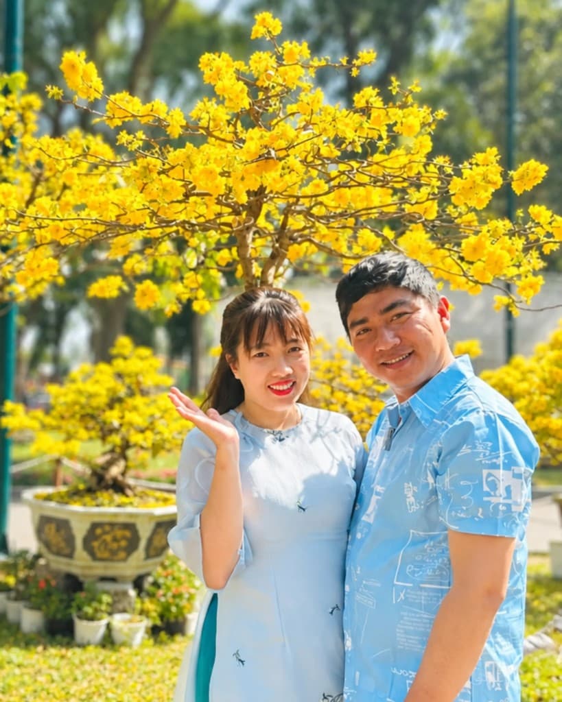Ngoc Ngan Ben Tre founders smiling together in front of a yellow flowering tree